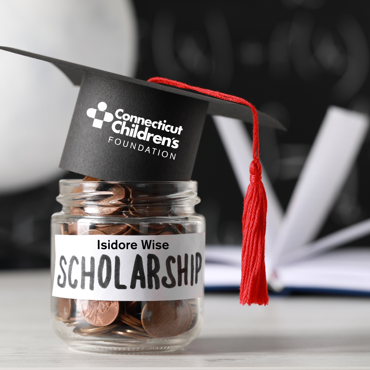 A tiny jar, labeled "Isidore Wise Scholarship" is filled with coins and is wearing a black graduation cap with red tassle.