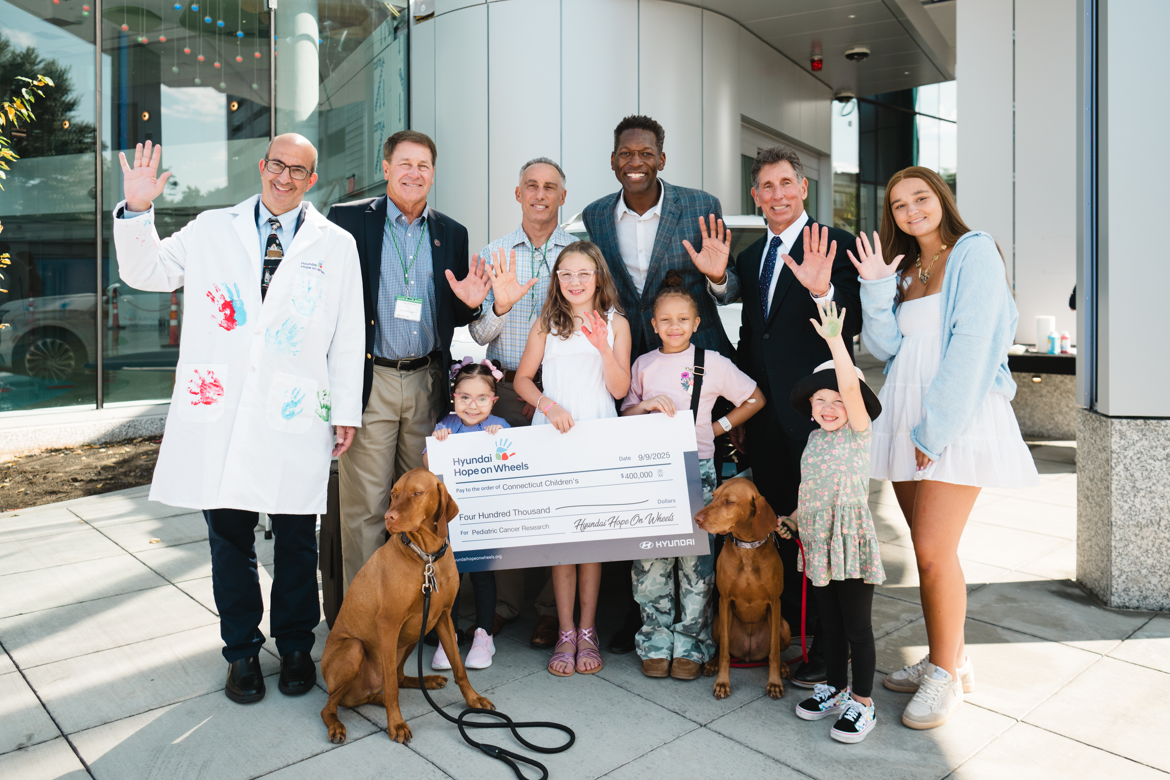 Patients, doctors, and Hyundai Hope on Wheels team members stand and show their hand with the donation check
