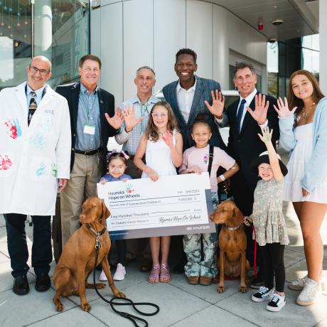 Patients, doctors, and Hyundai Hope on Wheels team members stand and show their hand with the donation check