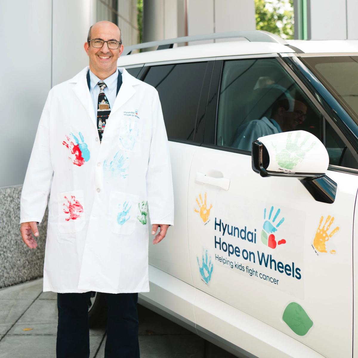 Dr. Isakoff wearing a lab coat next to Hyundai Hope on Wheels car