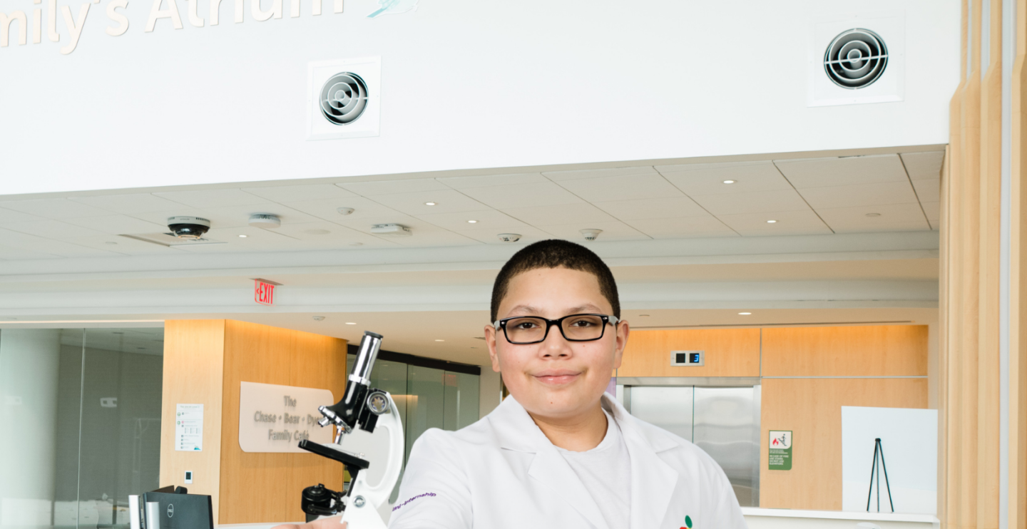 Elijah in a lab coat holding a microscope in the new tower