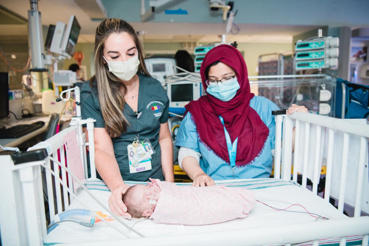 A nurse stands with a mother and her baby in the NICU